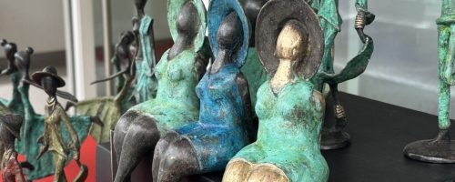 Gros plan sur des statuettes en bronze du Burkina Faso représentant des femmes assises avec des robes bleues et vertes.