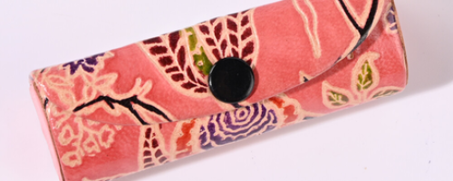 Petit étui en cuir écologique rose avec des motifs floraux de style batik et un bouton pression noir, sur fond blanc.